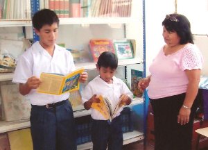 Niños de Educación Primaria repasan dos libritos de su Biblioteca y la Director PEDAGOGA Josefina La Rosa Huapaya ensaya una sonrisa de satisfacción